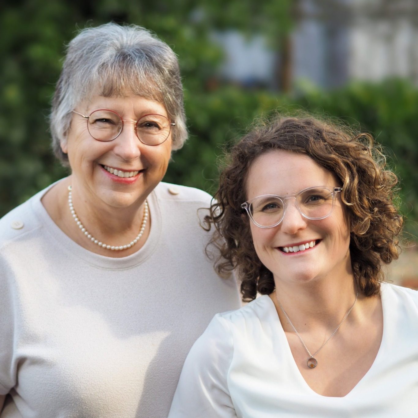 Zwei Frauen lächeln freundlich in einer hellen, grünen Umgebung.